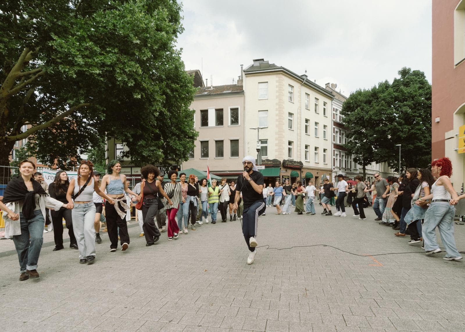 Ein großer Community-Dabke-Kreis tanzt draußen mit einem YallaDabka-Trainer