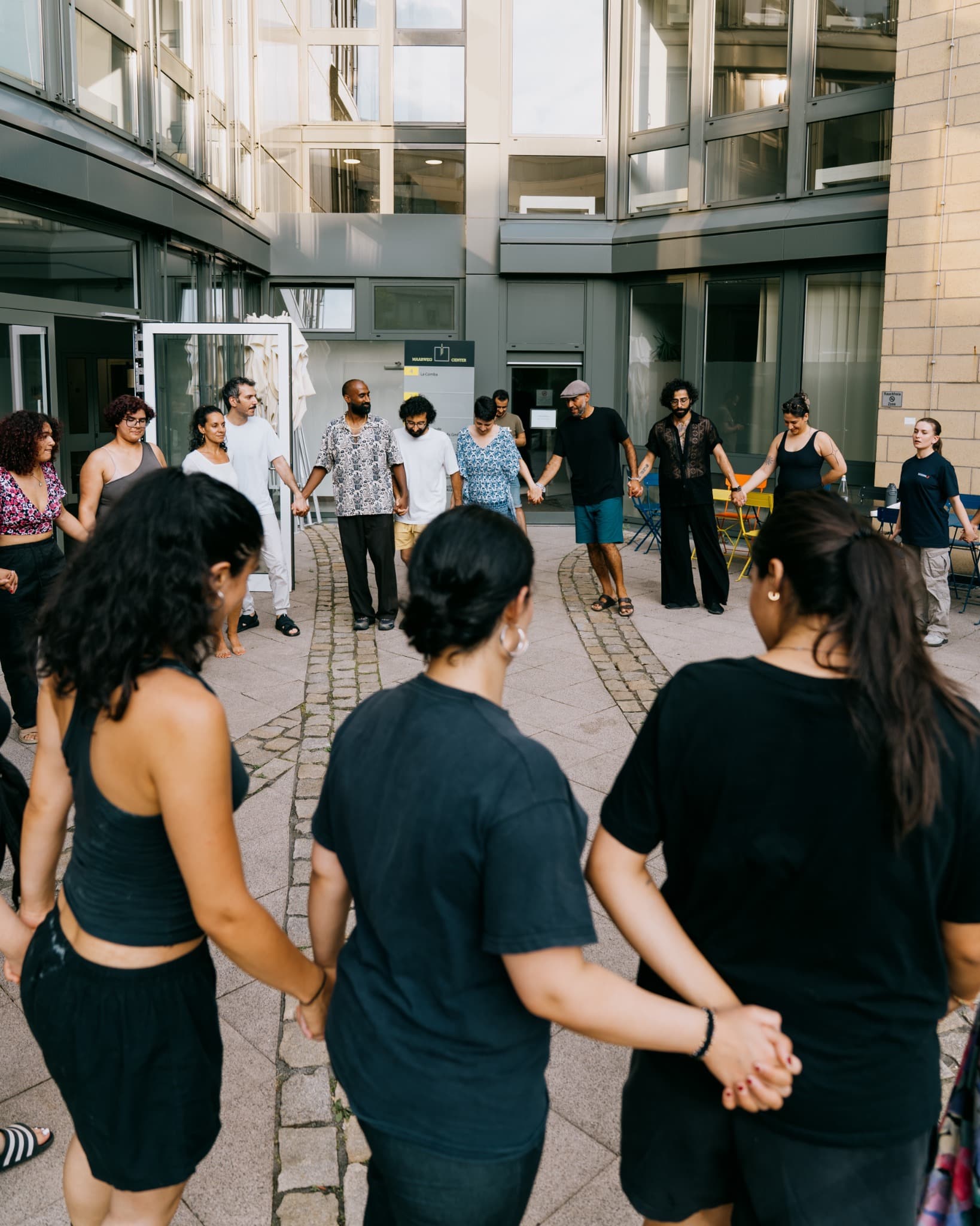 Eine vielfältige Gruppe hält sich während eines Dabke-Workshops im Kreis an den Händen